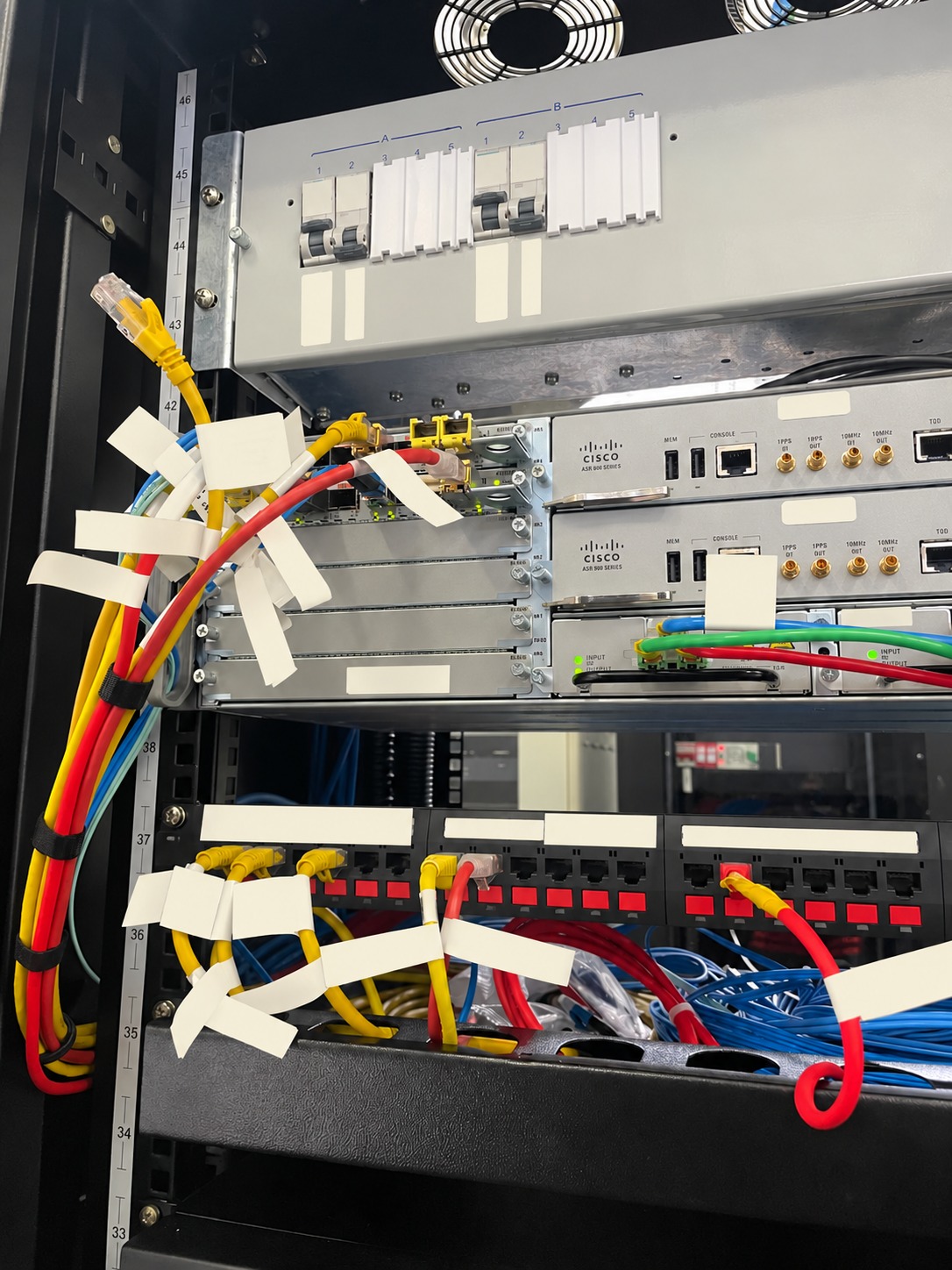 Rack de telecomunicações com roteadores, disjuntores e cabeamento identificado